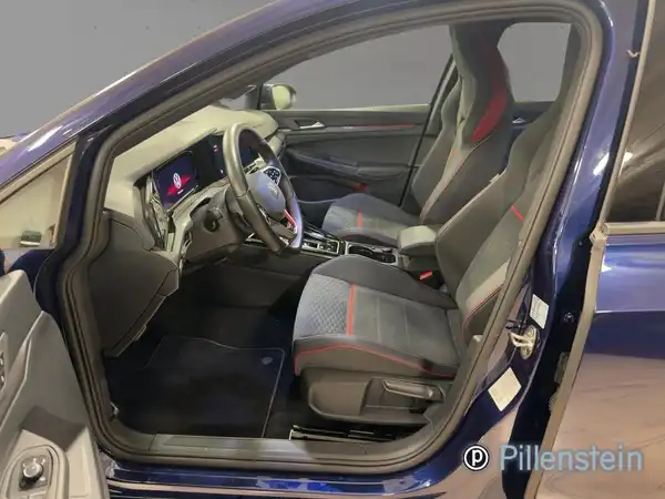 Das Bild zeigt das Innere eines blauen VW Golf GTI mit grauen Sitzen, die rote Akzente haben. Es ist eine Innenaufnahme des Fahrzeugs.