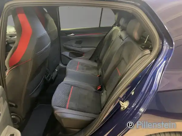 Das Bild zeigt den Innenraum des VW Golf GTI, speziell die Rücksitze, in blau mit schwarzem Interieur und roten Akzenten, außerdem ist ein Händlerlogo sichtbar.