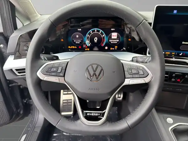 Eine Innenaufnahme des Fahrzeugs zeigt das Lenkrad und ein digitales Display. Das Interieur ist schwarz.