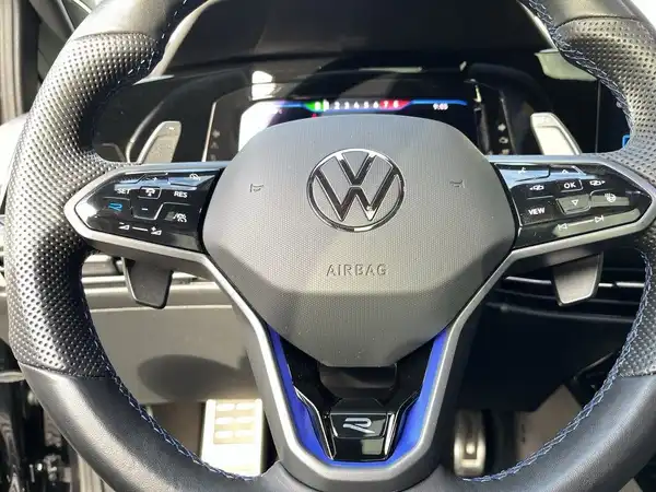 Das Bild zeigt das Lenkrad eines VW GOLF mit Details des Armaturenbretts. Es handelt sich um eine Innenaufnahme des Fahrzeugs, das Interieur ist schwarz mit blauen Akzenten.