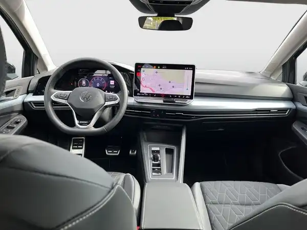 Das Bild zeigt das Innere eines VW Golf mit einem modernen schwarzen Interieur und einem digitalen Bildschirm, der Navigationsinformationen anzeigt.