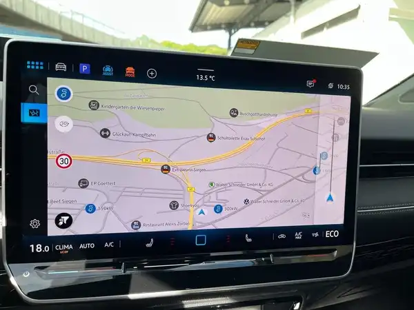 Das Bild zeigt den Innenraum eines Fahrzeugs mit einem großen Navigationsbildschirm, auf dem eine Karte mit Verkehrsinformationen zu sehen ist. Die Interieurfarbe ist schwarz.