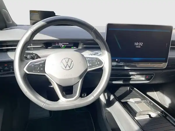 Innenaufnahme des VW ID.7 mit einem schwarzen Interieur, das Armaturenbrett und das Lenkrad sichtbar sind. Ein Bildschirm zeigt die Uhrzeit 10:32.