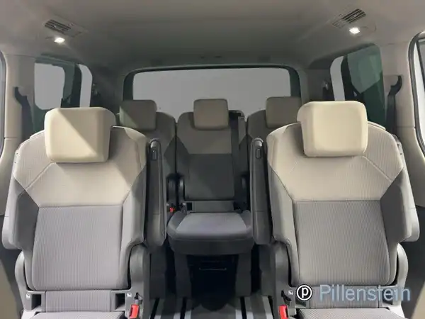 Innenaufnahme des Fahrzeugs VW Multivan in Grau mit mehreren Sitzen. Das Händlerlogo ist sichtbar.