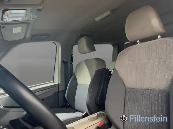 Das Bild zeigt das Innere eines VW Multivan mit grauen Sitzen. Die Sitze haben einen helleren Farbton auf der Sitzfläche. Der Händlername 'Pillenstein' ist im Bild sichtbar.