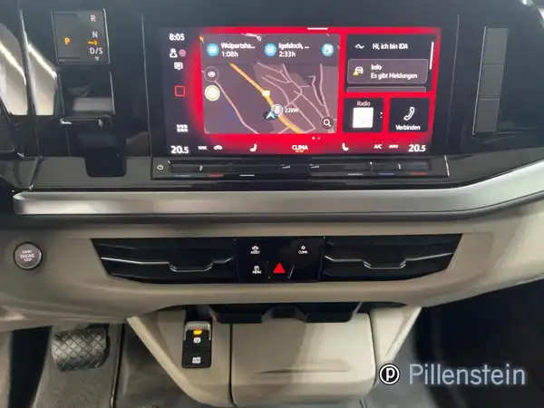 Das Bild zeigt den Innenraum eines VW Multivan mit einem schwarzen Interieur, insbesondere das Infotainment-System. Es sind markante Texteinblendungen sowie das Händlerinlogo vorhanden.
