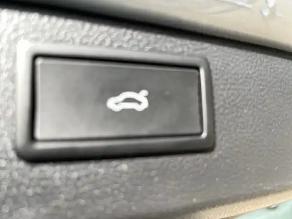 Aufnahme des Innenraums des Fahrzeugs, Blick auf einen Schalter. Der Schalter hat ein Auto-Symbol und die Innenfarbe ist schwarz.