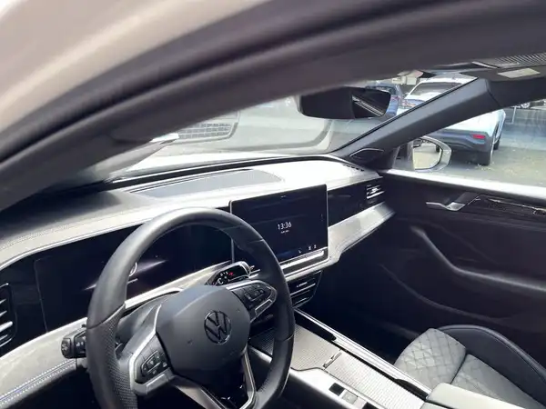 Das Bild zeigt das Innere eines VW Passats mit einem schwarzen und grauen Interieur. Das Armaturenbrett ist modern gestaltet, und es sind digitale Anzeigen sichtbar.