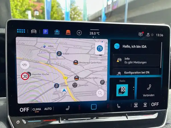 Das Bild zeigt das Interieur eines Fahrzeugs, aufgenommen von innen, mit einem Navigationsbildschirm, der Karteninformationen und Interaktionsoptionen anzeigt.
