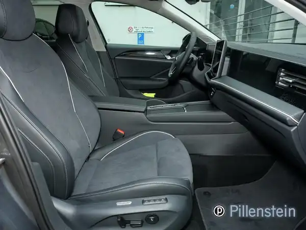 Das Bild zeigt den Innenraum eines VW Passat Variant in schwarzem Stoff mit grauen Nähten. Das Händlerlogo ist sichtbar.