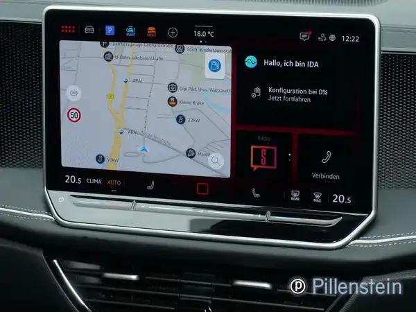 Das Bild zeigt das Innere eines VW Passat Variant mit einem Navigationsbildschirm. Der Bildschirm zeigt eine Kartenansicht und verschiedene Funktionen. Das Interieur ist in glänzendem Schwarz gehalten und es gibt ein Händlerlogo.