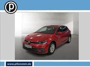 Das Bild zeigt einen roten VW Polo aus der Frontansicht. Das Fahrzeug ist in einem Ausstellungshintergrund platziert, wobei ein Händlerlogo sichtbar ist.