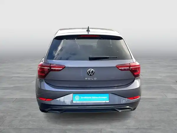 Das Bild zeigt einen grauen VW Polo von hinten. Auf dem Foto ist ein Händlerslogo eingeblendet und es sind markante Texteinblendungen zu sehen.