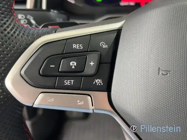 Ein Innenaufnahme des Fahrzeugs, zeigt das Lenkrad und die Steuerungselemente. Das Interieur ist schwarz. Das Händelerlogo ist sichtbar und es gibt markante Texteinblendungen.