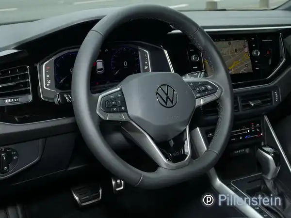 Das Bild zeigt das Innere eines Volkswagen Polo mit einem schwarzen Interieur. Es ist eine Aufnahme des Fahrzeuginnenraums, die das Lenkrad und das Armaturenbrett zeigt. Es befindet sich ein Händlerlogo im Bild.