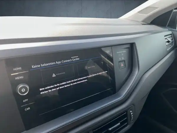 Das Bild zeigt das Innere eines VW Polo, insbesondere das Armaturenbrett mit einem Bildschirm. Die Innenfarbe ist schwarz und es sind markante Texteinblendungen vorhanden.