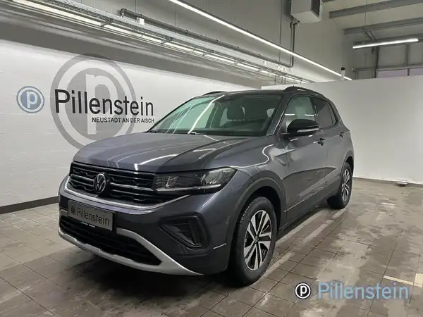 Das Bild zeigt einen grauen VW T-CROSS, aufgenommen von der Frontseite, mit dem Händlerlogo von Pillenstein im Hintergrund und markanten Texteinblendungen.