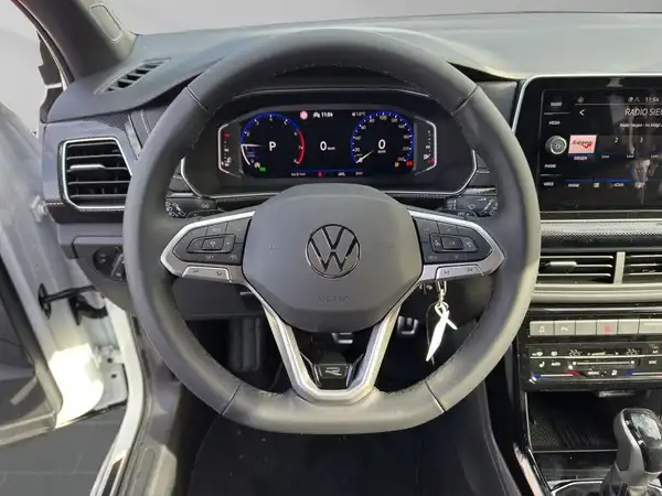 Das Bild zeigt das Cockpit eines VW T-CROSS mit einem modernen, schwarzen Interieur. Der Blickwinkel ist von innen auf das Lenkrad gerichtet.