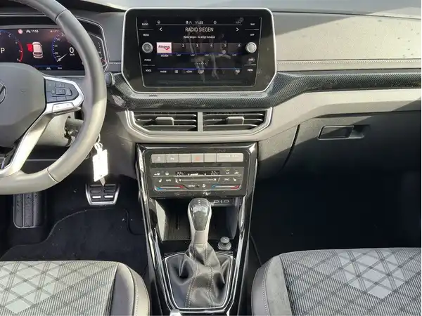 Das Bild zeigt das Innere eines VW T-CROSS mit einem modernen Cockpit, einem schwarzen Innenraum und einem Bildschirm an der Armaturentafel.
