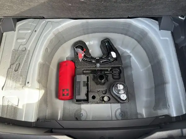 Das Bild zeigt den Kofferraum eines VW T-Cross von innen mit Werkzeugen und einem Verbandkasten in grauem Plastik.