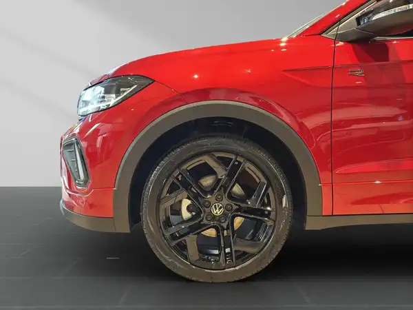 Das Bild zeigt einen roten VW T-CROSS von der Seite. Der Fokus liegt auf dem vorderen Rad und dem Karosseriedesign.