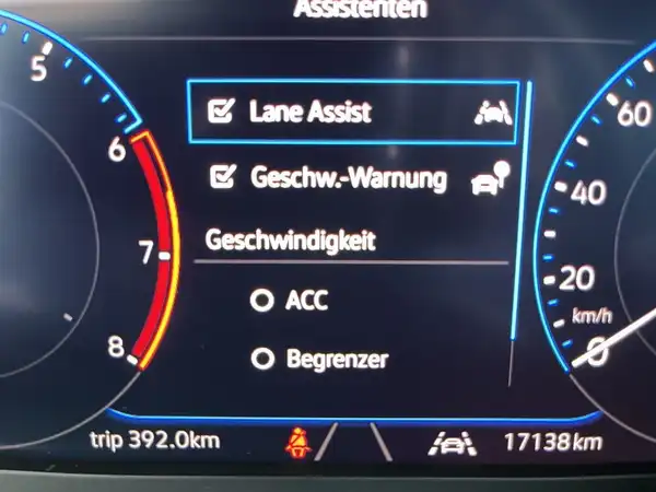 Das Bild zeigt das Armaturenbrett eines VW T-CROSS mit dem Bildschirm, auf dem verschiedene Fahrassistenzsysteme angezeigt werden. Das Interieur ist schwarz und es sind einige markante Texteinblendungen vorhanden.