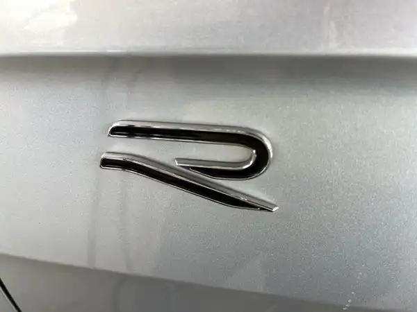 Das Bild zeigt das hintere Emblem eines silbernen Fahrzeugs, welches den Buchstaben 'R' darstellt.