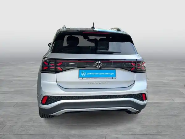 Das Bild zeigt einen VW T-CROSS von hinten in silberner Farbe, mit einem Händlerinformationslogo im unteren Bereich.