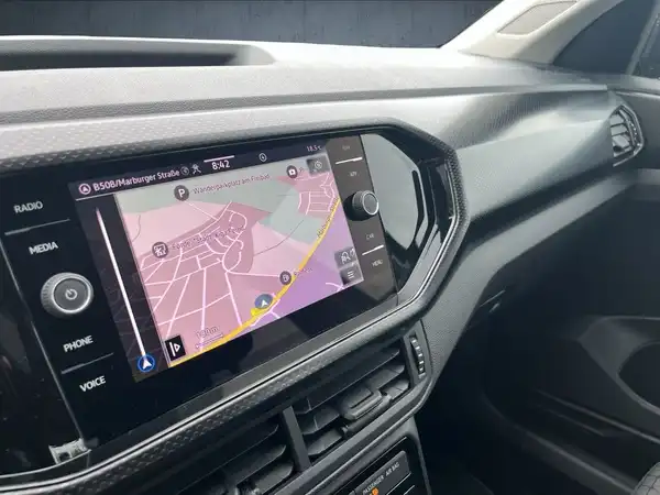 Das Bild zeigt das Innere des VW T-CROSS mit einem schwarzen Interieur und einem Bildschirm, auf dem Willkommensnachrichten angezeigt werden.