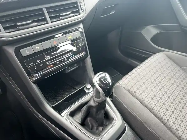 Das Bild zeigt das Innenraum eines VW T-CROSS mit einem schwarzen, strukturierten Interieur und Einrichtungen zur Steuerung des Infotainments.