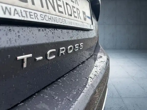 Das Bild zeigt die Rückansicht eines dunkelgrauen VW T-CROSS mit einem Händlerlogo und einem kurzen Schriftzug auf dem Nummernschild.