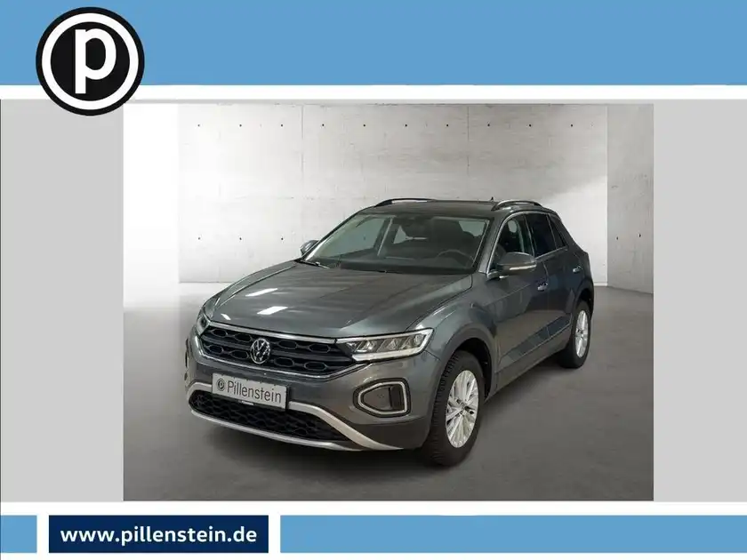 Das Bild zeigt einen grauen VW T-ROC von vorne. Es enthält das Händlerlogo und einige markante Texteinblendungen.