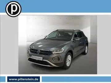 Das Bild zeigt einen grauen VW T-ROC von vorne. Es enthält das Händlerlogo und einige markante Texteinblendungen.