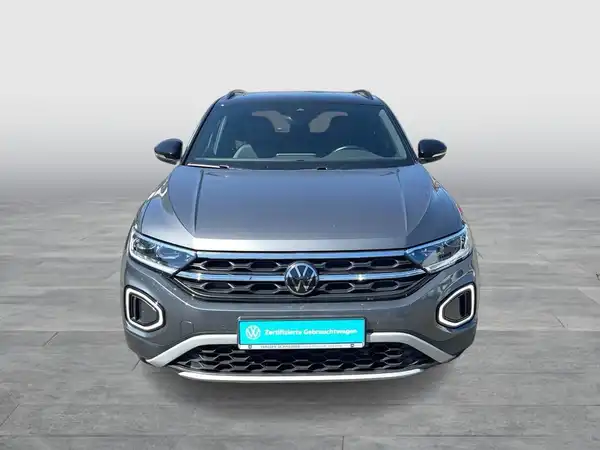 Das Bild zeigt einen grauen VW T-ROC aus der Frontalansicht. Es enthält das Logo des Händlers und eine Texteinblendung.