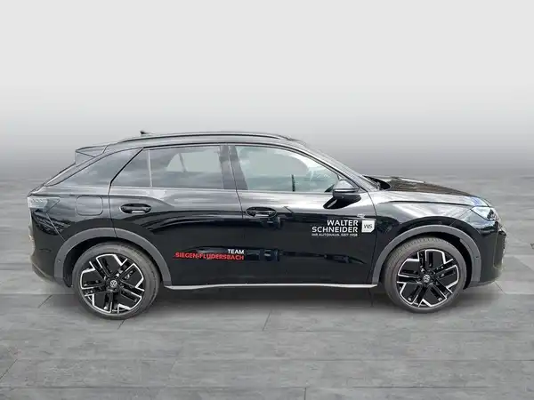 Das Bild zeigt einen schwarzen VW T-ROC von der Seite. Es sind Händlerlogos und Texteinblendungen sichtbar.
