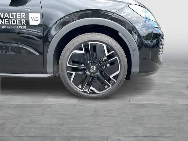 Das Bild zeigt einen VW T-ROC von der Seite. Das Fahrzeug ist schwarz und auf dem Bild ist ein Händlerlogo sowie markante Texteinblendungen zu sehen.