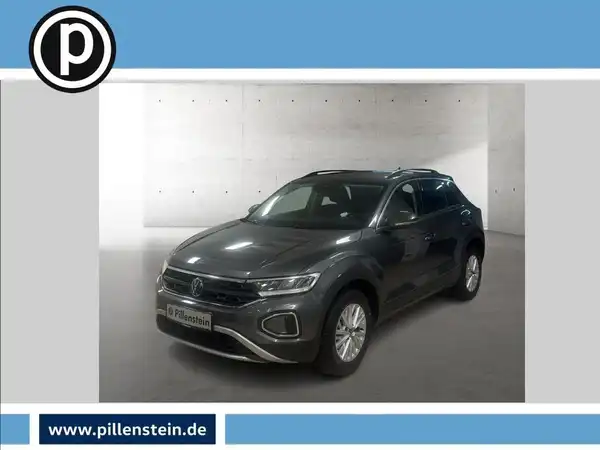 Das Bild zeigt einen VW T-ROC in grauer Farbe, aufgenommen von der Seite. Es sind das Händlerlogo und markante Texteinblendungen im Bild enthalten.