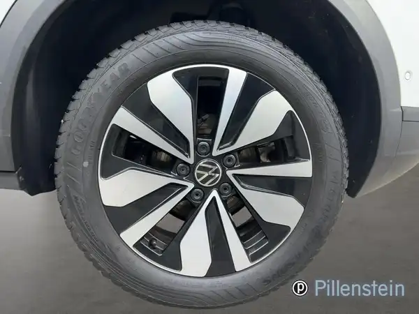 Das Bild zeigt eine Nahaufnahme des Reifens und der Felge eines VW T-ROC aus der Seitenansicht. Es ist ein Händlerlogo sichtbar.