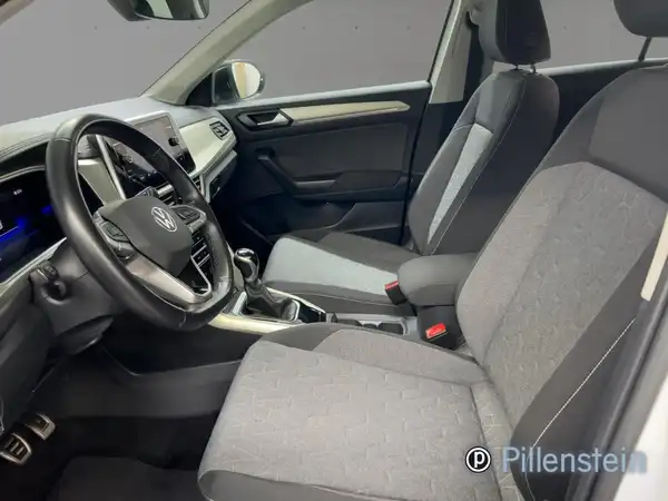 Das Bild zeigt den Innenraum eines VW T-ROC aus der Sicht des Fahrers. Die Sitze sind grau gepolstert und das Händlerlogo von Pillenstein ist sichtbar.