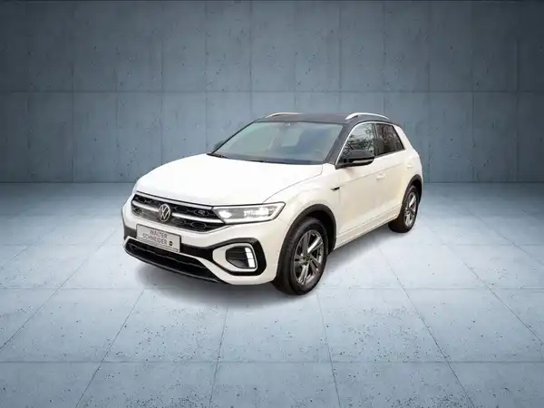 Das Bild zeigt einen weißen VW T-ROC aus der Frontansicht, mit dem Händlerinformationslogo im unteren Bereich.