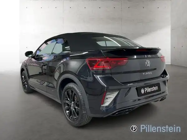 Das Bild zeigt einen schwarzen VW T-ROC Cabriolet aus der Rückansicht. Auf dem Fahrzeug ist das Händlerlogo 'Pillenstein' zu sehen.
