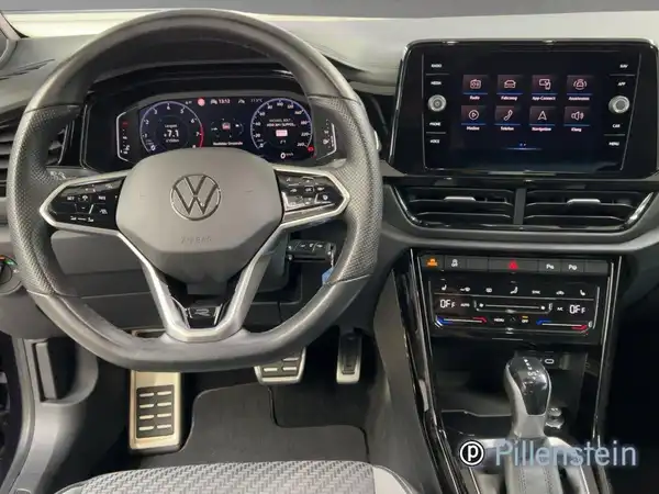 Das Bild zeigt das Innere eines VW T-ROC CABRIOLET mit einem schwarzen und grauen Interieur und ist eine Innenaufnahme. Es enthält das Händlerlogo. Es sind markante Texteinblendungen vorhanden.