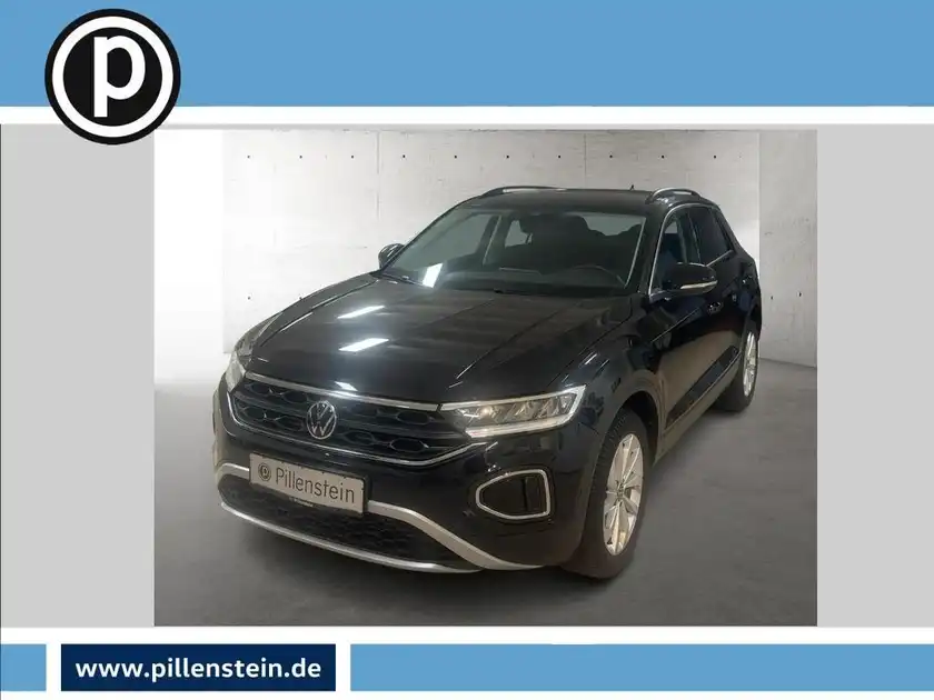 Das Bild zeigt einen schwarzen VW T-ROC von vorne. Es gibt ein Händlerlogo in der oberen linken Ecke.