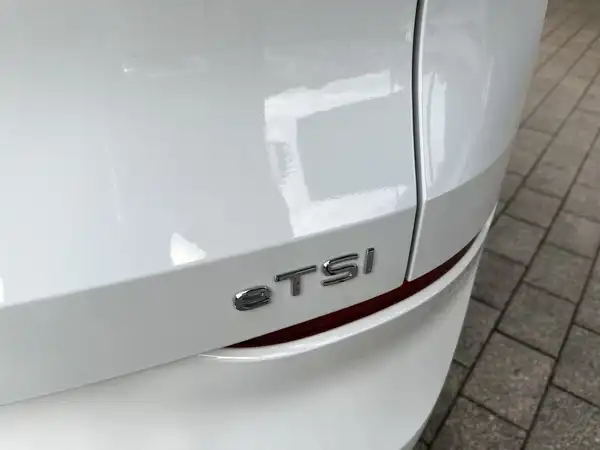 Das Bild zeigt die Rückansicht eines weißen VW T-ROC mit einem klaren Blick auf das TSI-Emblem.