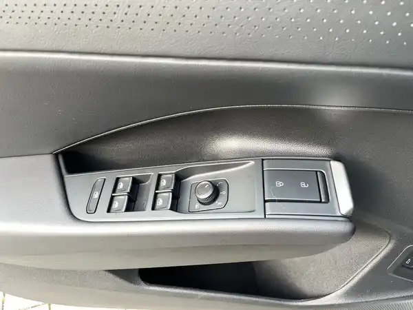 Das Bild zeigt die Türverkleidung eines VW T-ROC mit Bedienelementen für Fensterheber in schwarzer Farbe.