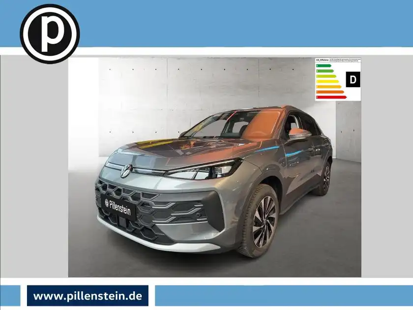 Das Bild zeigt einen VW T-ROC aus der Frontansicht, in grauer Farbe. Es enthält das Händlerlogo und einige markante Texteinblendungen.