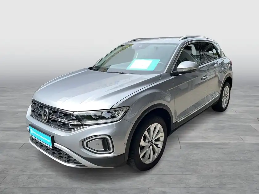 Das Bild zeigt einen silbernen VW T-Roc von der Seite. Es handelt sich um ein normales Fahrzeugbild, das einige markante Texteinblendungen enthält.