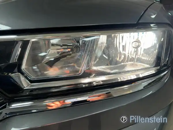 Nahaufnahme des Frontscheinwerfers eines grauen VW T-ROC. Das Bild zeigt den Scheinwerfer und die umliegenden Chromelemente.