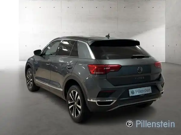 Das Bild zeigt einen grauen VW T-ROC von hinten. Das Fahrzeug ist in einem Innenraum mit neutraler Wandfarbe aufgenommen.