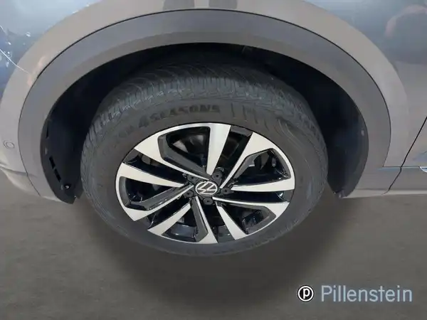 Das Bild zeigt die Seite eines VW T-ROC mit dem Fokus auf der Felge und dem Reifen. Das Fahrzeug ist grau.